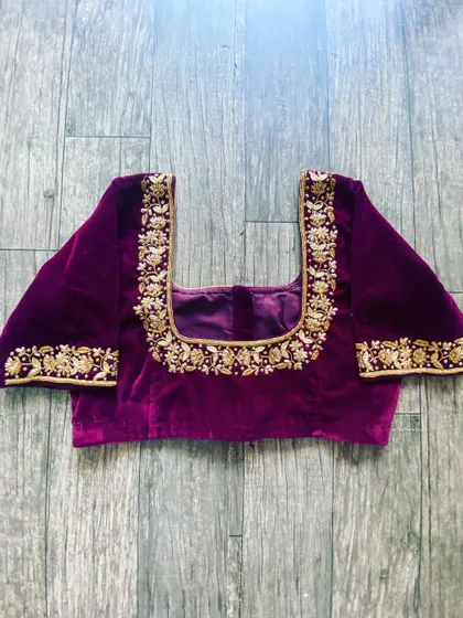 This purple velvet blouse has a square neckline with gold floral embroidery. The same pattern is repeated on the sleeve cuffs for a balanced design.