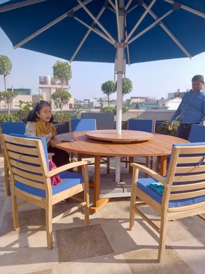 Another rooftop garden, this one featuring a large round dining table with blue cushions and a matching blue umbrella. The space is perfect for outdoor dining with a view.