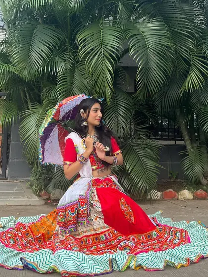 Accessorized with a small, colorful umbrella, this red and white chaniya choli is ready for a festive photo op.