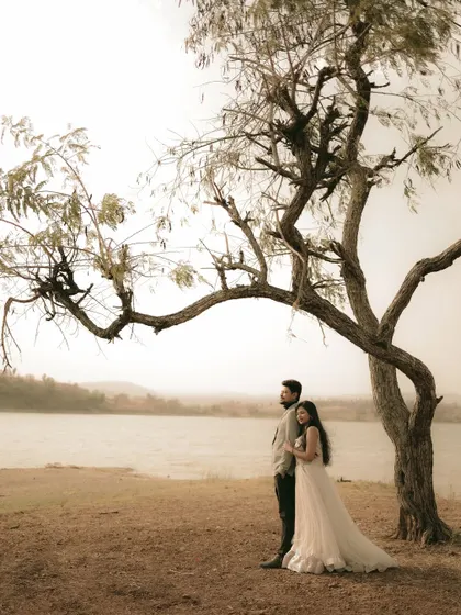 A couple finding a quiet moment under a sprawling tree by the lake. This wide shot emphasizes the beauty of nature as a setting for your love story.