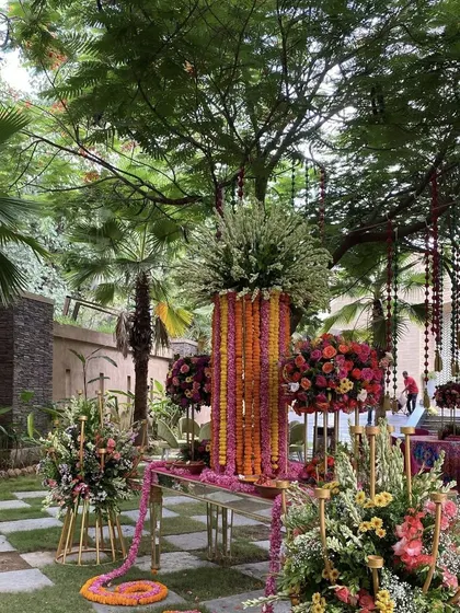 For grander celebrations at home, we specialize in creating lavish floral installations. This garden setup features towering arrangements of marigolds and lush bouquets of roses and mixed florals, demonstrating our expertise in large scale floral artistry. We use mirrored tables and elegant stands to add a touch of glamour to the outdoor space.