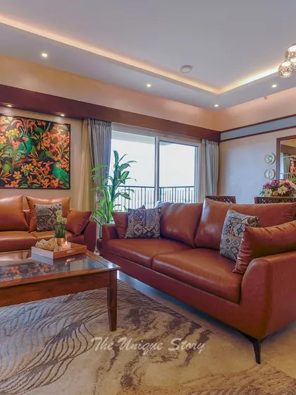 We transformed this living room into a cozy Indian contemporary space. The design features rich tan leather sofas, a custom wooden TV unit with open shelving supported by metal rods, and vibrant artwork to create a warm and inviting atmosphere.