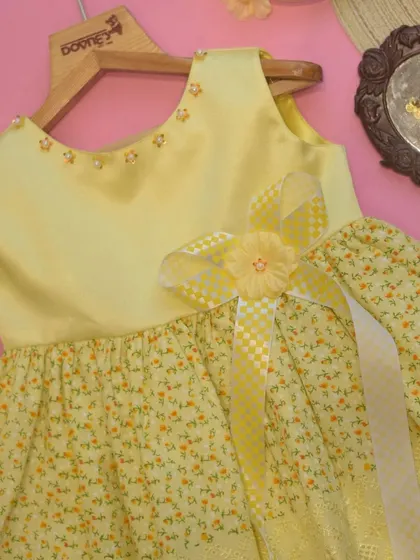 A closer look at the sunny yellow dress, highlighting the pearl details along the neckline and the multi-layered bow at the waist.