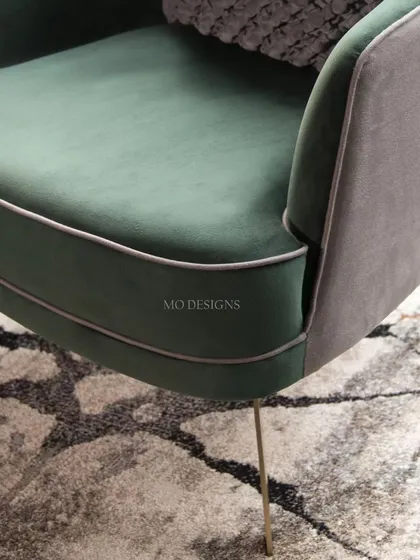 A detail of our Verdure Armchair, showcasing the rich emerald green velvet and contrasting grey back. The sleek, gold-toned legs and fine piping add a touch of richness, creating a piece that speaks of nature's poise and serenity.