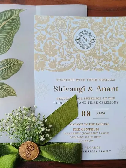 A full view of the sophisticated engagement invitation for Shivangi and Anant. The design features a classic floral damask pattern in gold, a modern monogram, and a translucent vellum wrap with a rich green velvet ribbon, creating a look of timeless elegance.