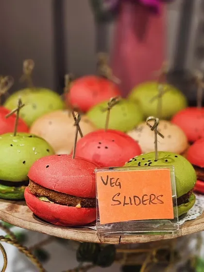Our colorful veg sliders, made with beetroot and spinach-infused buns, add a pop of color and flavor to this hi-tea grazing table. They look like macarons but are savory delights!