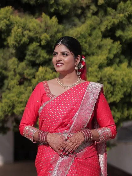 A smiling bride in her red saree, her hands beautifully decorated with a dark and lovely mehendi stain.