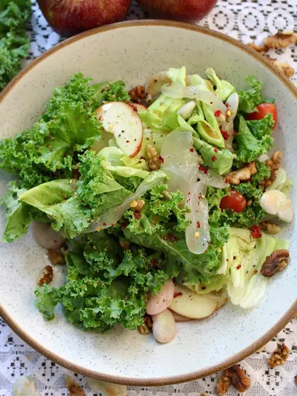 A top-down view of the Double Beans, Kale & Ice Apple Salad, showcasing the vibrant mix of leafy kale, red cherry tomatoes, and creamy white beans.