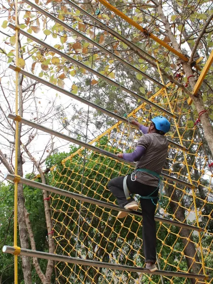 A guest makes their way up the climbing net, fully harnessed and secured. Safety is our top priority, so you can focus on the fun and the challenge.