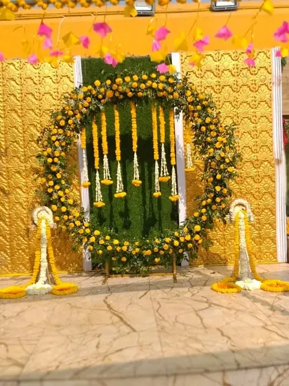 An outdoor stage with a circular floral backdrop made of marigolds and jasmine. The stage is framed with marigold garlands, perfect for a Haldi or Mehendi ceremony.