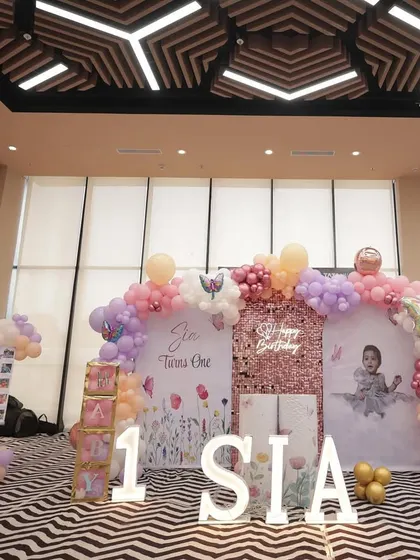 A grand butterfly-themed setup for Sia's first birthday. The decor features a large balloon arch in pastel shades, a sequin wall, and personalized backdrops against a modern chevron-patterned floor.