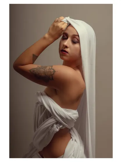 A serene and artistic portrait of a model draped in white fabric. Her closed eyes and gentle pose convey a sense of peace and introspection.