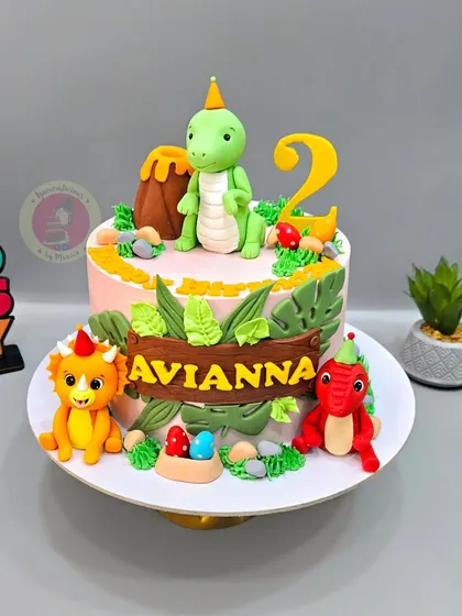 A cute dinosaur-themed cake for Avianna's 2nd birthday, featuring friendly fondant dinosaurs, a volcano, and jungle leaves.