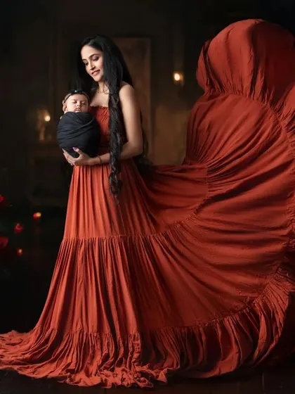 A dramatic and stunning portrait of a mother in a flowing red gown, holding her newborn baby close.