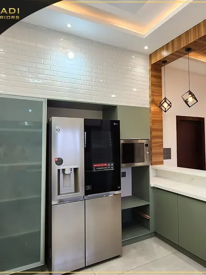 This kitchen design seamlessly integrates a large side-by-side refrigerator. The combination of olive green cabinets, white countertops, and a brick-patterned backsplash creates a modern yet rustic feel.
