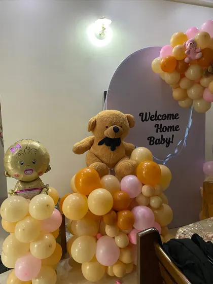 A close-up of the 'Welcome Home Baby' decor, showing the teddy bear and baby-themed foil balloon nestled in the pastel balloon arrangement.
