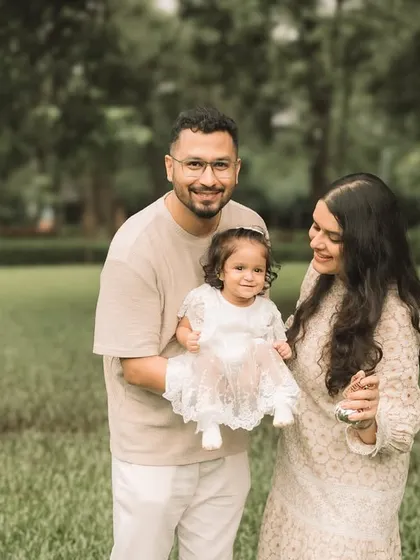 A happy family of three posing for a portrait in a lush green field. Their coordinated neutral outfits look perfect.