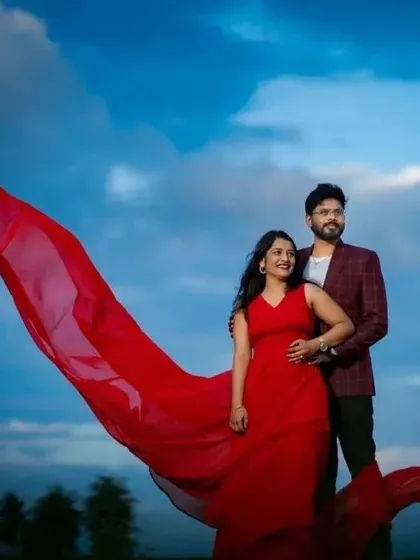 The red trail of the dress billows against a dramatic blue sky, creating a stunning visual for this couple's photoshoot.