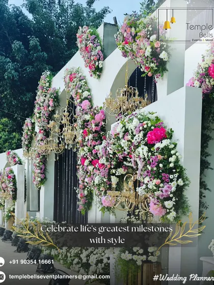 We transform venues into masterpieces. This decor features a white facade adorned with cascading pink florals and ornate golden chandeliers for a luxurious feel.