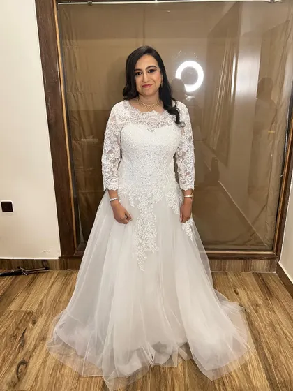 A full-length shot of our beautiful bride Meghana in her elegant white wedding gown. The long lace sleeves and flowing tulle skirt create a timeless and romantic silhouette.