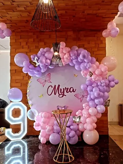 A charming butterfly theme for a 9th birthday. This design uses a soft pink and purple palette for the balloon arch, a personalized backdrop, and a large light-up number '9'.