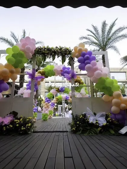 Another view of the butterfly party entrance, showing the full arch with its colorful balloons and floral arrangements against the evening sky.