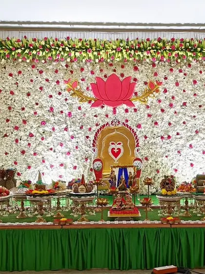 A baby shower setup with a green and white floral backdrop, featuring a large lotus motif and a full display of traditional plates.