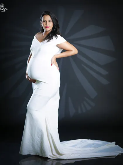 A full-length portrait in our classic white fitted gown. This off-the-shoulder dress features a long train, adding a touch of Hollywood glamour to your maternity photos.