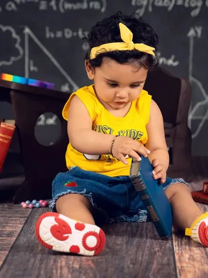 A baby girl is deeply focused on her "studies," playing with a brush in front of a chalkboard backdrop.