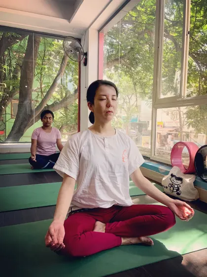 A student finds a moment of peace in a seated meditation pose, with the lush greenery outside the window.