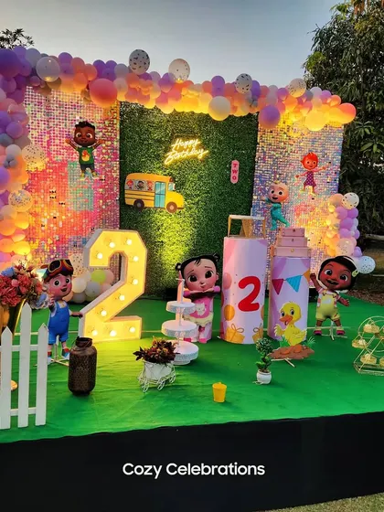 An outdoor Cocomelon party featuring a sequin and greenery backdrop. The light-up number 2 and various character cutouts make it a fun and interactive space.