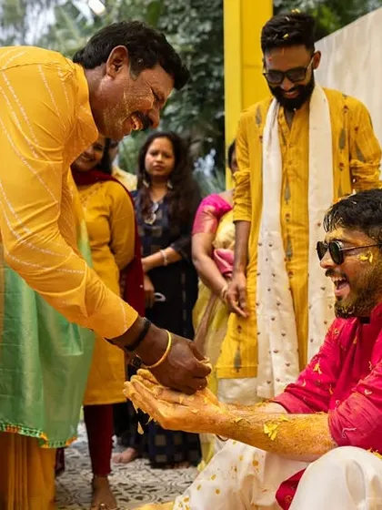 Friends and family share a laugh while applying turmeric to the groom during a joyous Haldi celebration.