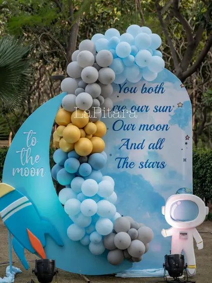 A crescent moon photo op with a rocket ship, surrounded by a cloud of balloons. The sign reads 'To the moon', perfect for capturing adventurous photos.