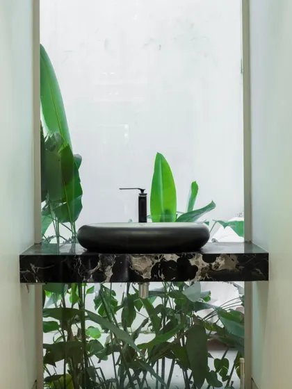 A minimalist powder room where the sink is set against a window overlooking a private green space. This design brings a touch of nature indoors, creating a refreshing and serene experience.