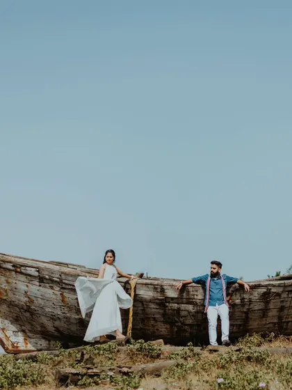 A wide-angle shot of a couple posing on a rustic, abandoned boat in Alibag. This unique prop adds a powerful, story-driven element to their beach pre-wedding shoot.