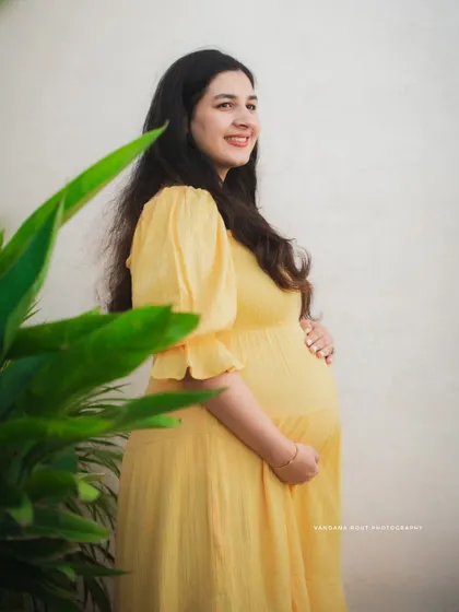 A beautiful solo portrait of a mother-to-be in a sunny yellow dress, smiling as she holds her bump. The focus is on her radiant glow amidst natural surroundings.