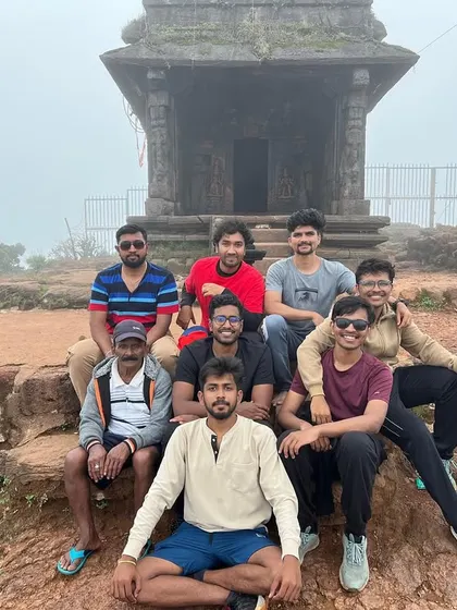 A group rests at a small temple structure on a misty hilltop during the Kodachadri trek.