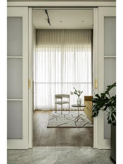 A view into the den room through the sliding pocket doors. The design is both modern and timeless, with warm tones and brass accents creating a luxurious and comfortable atmosphere.