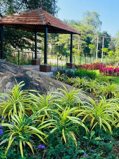 A beautiful park landscape featuring a mix of colorful foliage and green plants. We designed this space with a gazebo nestled among natural rock formations, creating a picturesque spot to enjoy the outdoors.