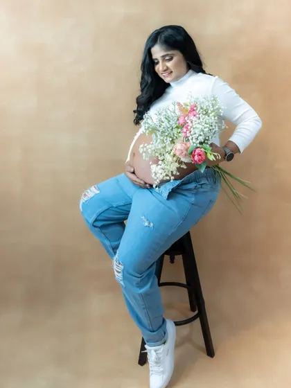 A casual and cute studio portrait of a mom-to-be in ripped jeans and a white top, holding a bouquet of flowers.