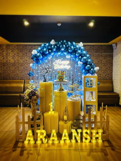 A stunning blue-themed first birthday party. The deep blue and light blue balloon arch is paired with a silver shimmer curtain, a neon sign, and a full set of props for a grand celebration.