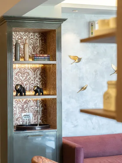 This exquisite display cabinet features a damask-patterned wallpaper on the back panel, creating a rich, textured backdrop for the decor items within. The fluted details on the cabinet exterior add another layer of sophistication.