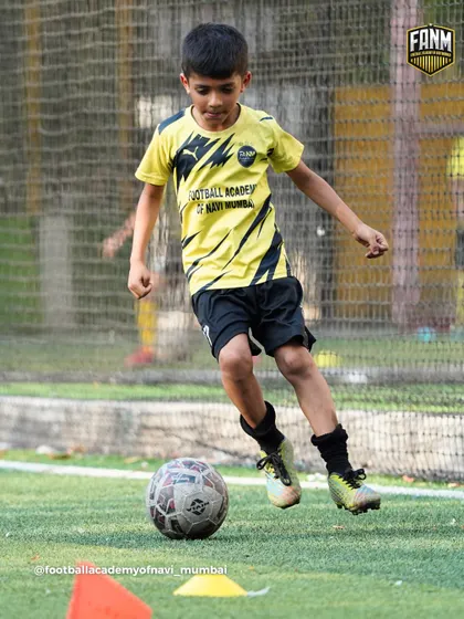 A young player practices his dribbling skills, keeping the ball close as he moves past a cone. Mastering ball control is the first step to becoming a confident player.