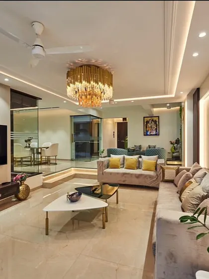 This living room design features a split-level layout, creating distinct zones for seating and passage. We used a grand chandelier and continuous profile lighting to unify the space, while the glass partition maintains a visual connection to the dining area.