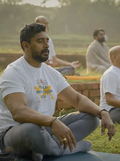 A participant meditates with serene focus during the World Meditation Day event. The calm morning light and natural surroundings enhance the depth of the experience.