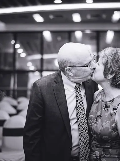 A sweet kiss between an older couple at the wedding, captured in a timeless black and white photograph.