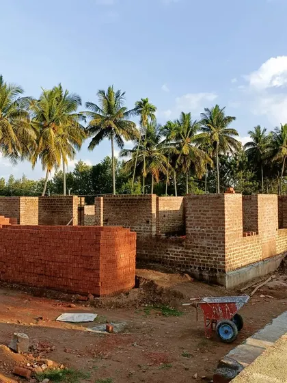 Stacks of bricks and rising walls at the Srirangapatna site. This image captures the raw energy and potential of a construction site where a building is taking shape from the ground up.