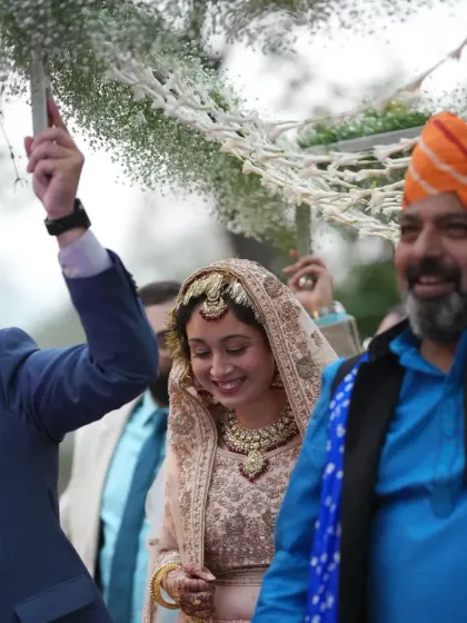 The bride's joyful entry under a 'phoolon ki chadar' made of baby's breath, surrounded by smiling family and friends.