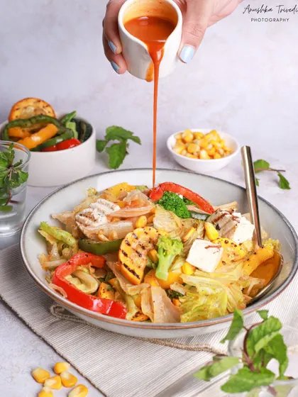 A healthy and colourful salad with grilled chicken and vegetables. The action of pouring the dressing adds a dynamic element to this fresh and vibrant shot.