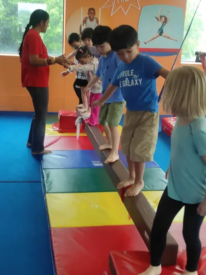 A coach guides a line of children across the balance beam, ensuring each child feels secure as they practice this important skill.